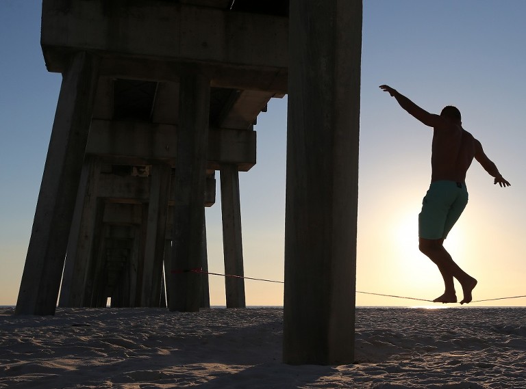 Andrew Heymann walks a slackline beneath the M.B. Miller County Pier in Panama City Beach. Slacklining differs from tight wires and tightropes in that they are tensioned to create a line with bounce and stretch like a long and thin trampoline. (Panama City Photographer | Andrew Wardlow)