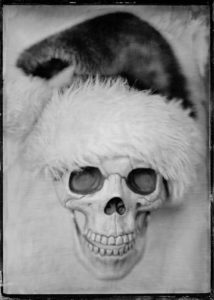 Tintype or wet plate photograph of a skull wearing a Santa hat.