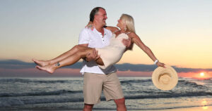 A man carries a woman at sunset as they are photographed by Panama City Beach photographer Andrew Wardlow.