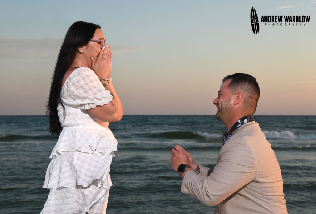 A woman shows surprise as a man proposes to her during a beach proposal photo session in Panama City Beach, Florida.