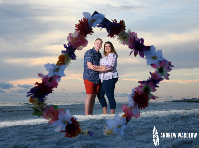 A couple is framed by a photo frame in the sand after getting engaged during a beach proposal photo session in Panama City Beach, Florida.