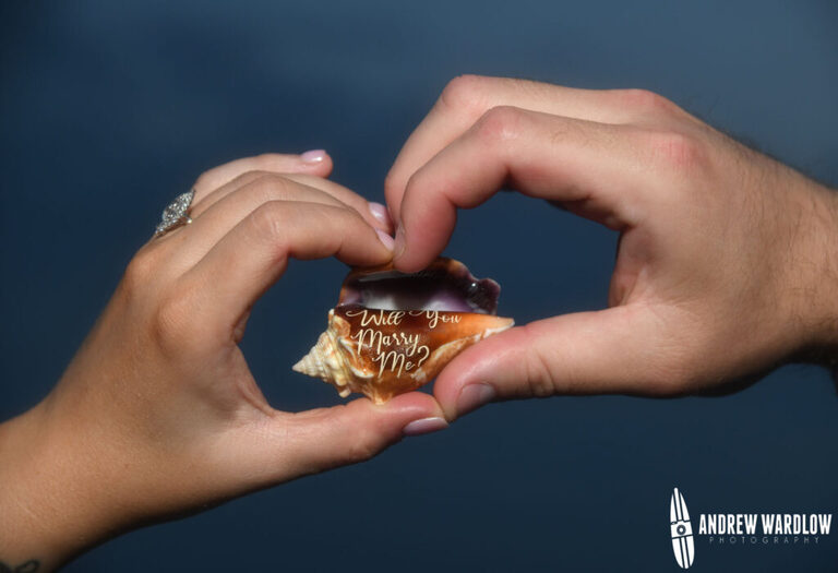 A man and a woman hold a shell that says, "Will you Marry Me?" during a beach proposal photo session in Panama City Beach, Florida.